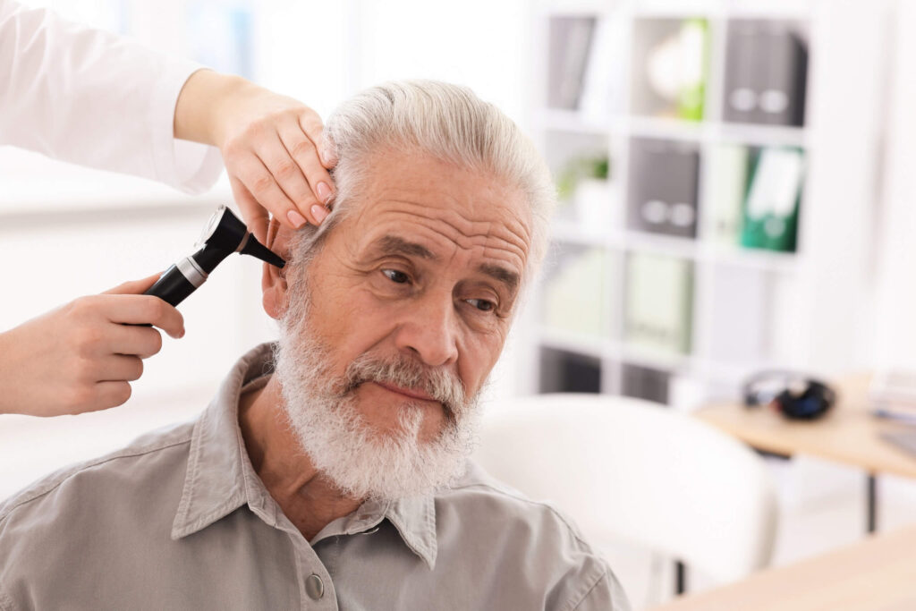 Clinician examining an older man’s ear with an otoscope during a medical check-up.