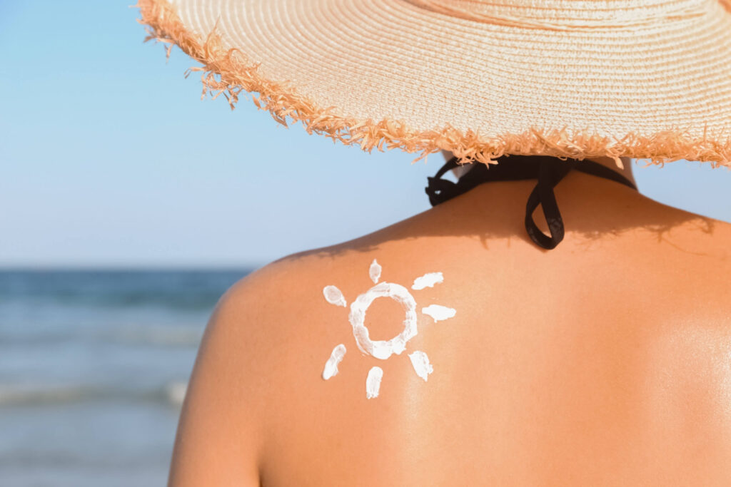 Person wearing a wide-brim hat at the beach with sunscreen applied to the shoulder in a sun shape